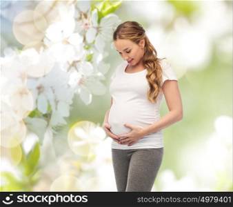 pregnancy, motherhood, people and expectation concept - happy pregnant woman touching her big belly over natural spring cherry blossom background. happy pregnant woman touching her big belly