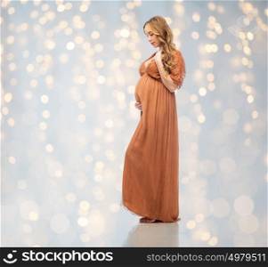 pregnancy, motherhood, people and expectation concept - happy pregnant woman touching her big belly over holidays lights background. happy pregnant woman touching her big belly