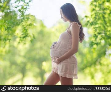 pregnancy, motherhood, people and expectation concept - happy pregnant woman touching her belly over green natural background. happy pregnant woman touching her belly