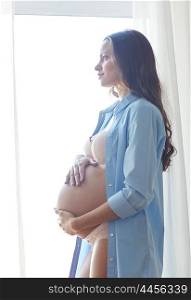 pregnancy, motherhood, people and expectation concept - happy pregnant woman with big bare tummy near window at home
