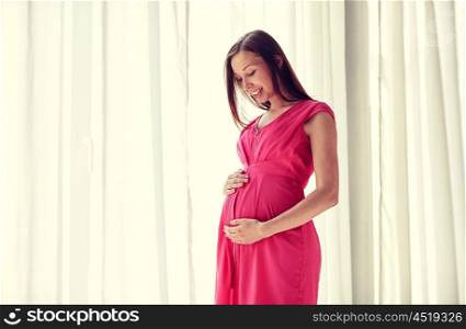 pregnancy, motherhood, people and expectation concept - happy pregnant woman with big tummy looking through window at home