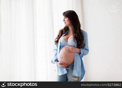 pregnancy, motherhood, people and expectation concept - happy pregnant woman with big bare tummy looking through window at home. happy pregnant woman with big tummy at home