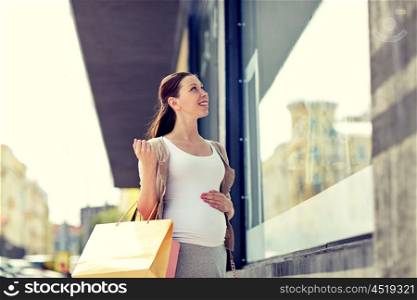pregnancy, motherhood, people and expectation concept - happy smiling pregnant woman with shopping bags at city street
