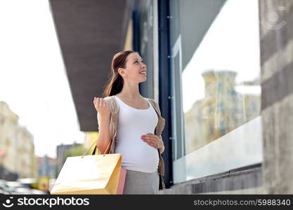 pregnancy, motherhood, people and expectation concept - happy smiling pregnant woman with shopping bags at city street