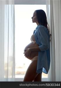 pregnancy, motherhood, people and expectation concept - silhouette of happy pregnant woman with big bare tummy near window at home