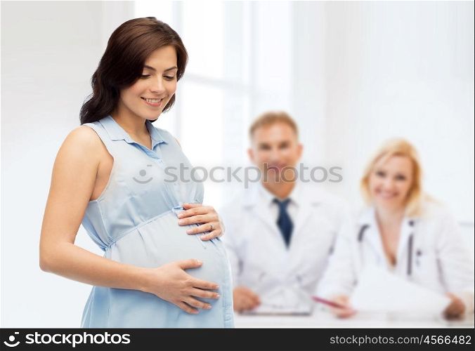 pregnancy, motherhood, people, medicine and fertility concept - happy pregnant woman touching her big belly over medics at maternity hospital background