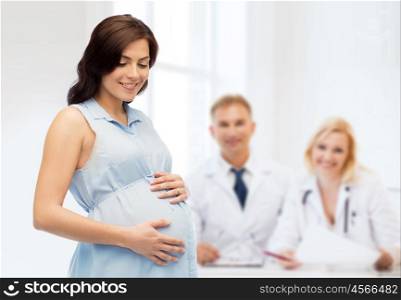 pregnancy, motherhood, people, medicine and fertility concept - happy pregnant woman touching her big belly over medics at maternity hospital background