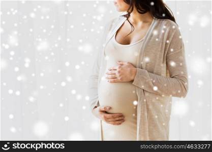 pregnancy, motherhood, people, winter and expectation concept - close up of pregnant woman with big belly looking to window over snow
