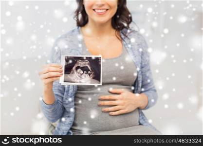 pregnancy, motherhood, people, winter and medicine concept - close up of happy pregnant woman holding at ultrasound image at home over snow