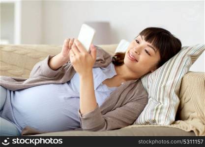 pregnancy, motherhood, technology and people concept - happy pregnant asian woman with smartphone lying on sofa at home. happy pregnant woman with smartphone at home