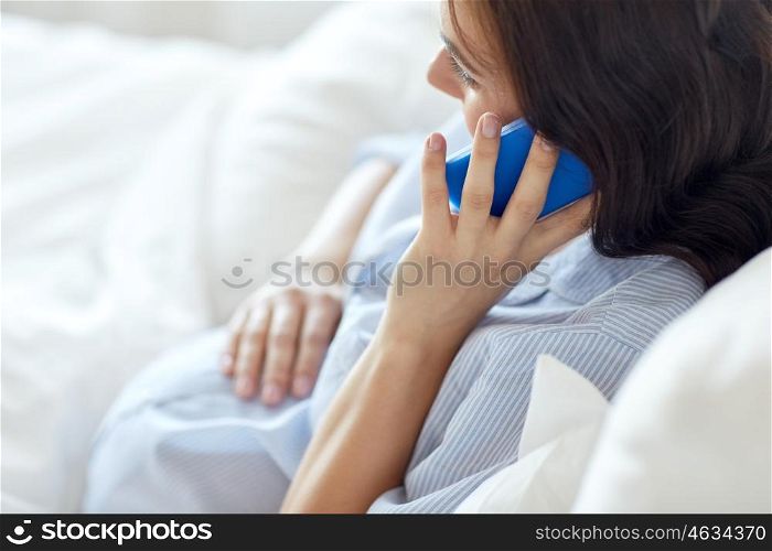 pregnancy, motherhood, technology, people and expectation concept - close up of happy pregnant woman calling on smartphone in bed at home