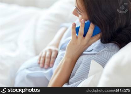 pregnancy, motherhood, technology, people and expectation concept - close up of happy pregnant woman calling on smartphone in bed at home