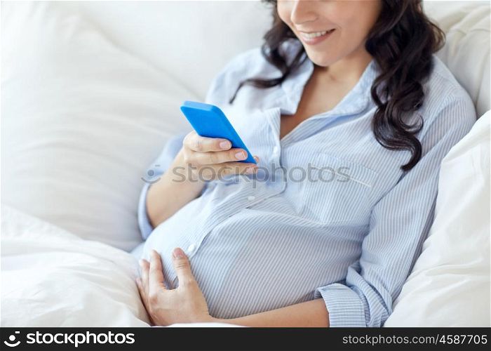 pregnancy, motherhood, technology, people and expectation concept - close up of pregnant woman with smartphone in bed at home