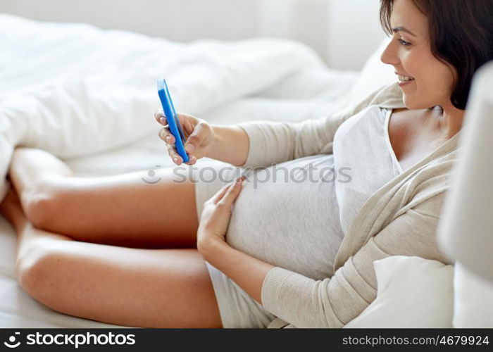 pregnancy, motherhood, technology, people and expectation concept - close up of pregnant woman with smartphone in bed at home