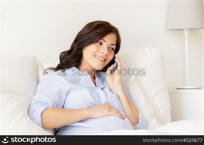 pregnancy, motherhood, technology, people and expectation concept - happy pregnant woman calling on smartphone in bed at home