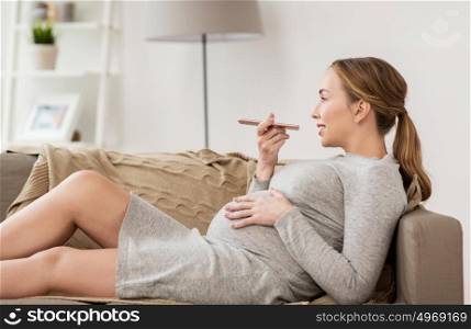pregnancy, motherhood, technology, people and expectation concept - happy pregnant woman using voice command recorder or calling on smartphone at home. pregnant woman using voice recorder on smartphone