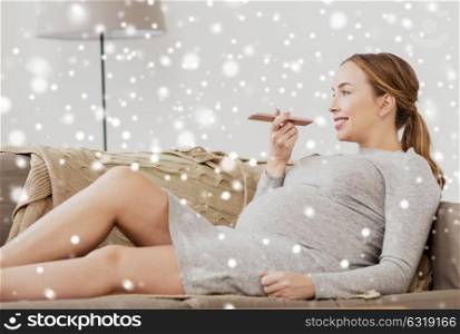 pregnancy, motherhood, technology, people and expectation concept - happy pregnant woman using voice command recorder or calling on smartphone at home over snow. pregnant woman using voice recorder on smartphone