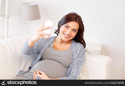 pregnancy, motherhood, technology, people and expectation concept - happy pregnant woman with smartphone taking selfie at home