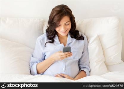 pregnancy, motherhood, technology, people and expectation concept - happy pregnant woman with smartphone in bed at home