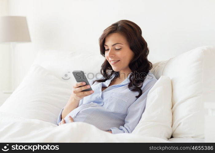 pregnancy, motherhood, technology, people and expectation concept - happy pregnant woman with smartphone in bed at home