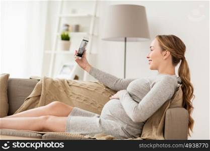 pregnancy, motherhood, technology, people and expectation concept - happy pregnant woman with smartphone taking selfie at home. pregnant woman taking smartphone selfie at home