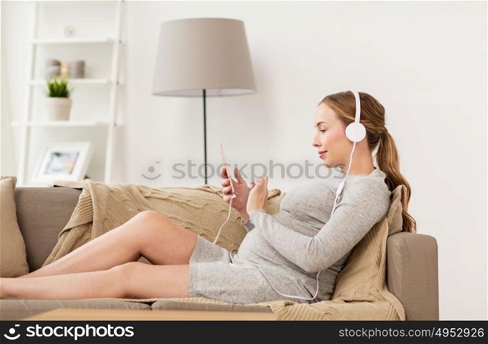 pregnancy, motherhood, technology, people and expectation concept - happy pregnant woman with smartphone and headphones listening to music at home. pregnant woman with smartphone and headphones