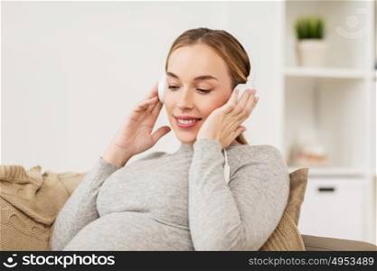 pregnancy, motherhood, technology, people and expectation concept - happy pregnant woman with headphones listening to music at home. pregnant woman with headphones listening to music