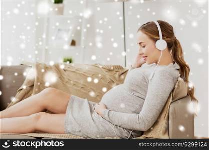 pregnancy, motherhood, technology, people and expectation concept - happy pregnant woman with headphones listening to music at home over snow. pregnant woman with headphones listening to music