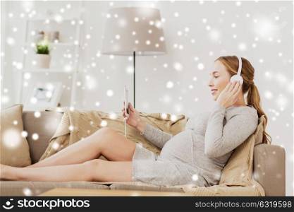pregnancy, motherhood, technology, people and expectation concept - happy pregnant woman with smartphone and headphones listening to music at home over snow. pregnant woman with smartphone and headphones