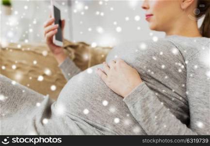 pregnancy, motherhood, technology, people and expectation concept - happy pregnant woman with smartphone at home over snow. happy pregnant woman with smartphone at home