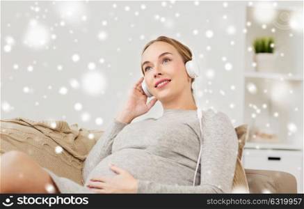 pregnancy, motherhood, technology, people and expectation concept - happy pregnant woman with headphones listening to music at home over snow. pregnant woman with headphones listening to music
