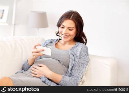 pregnancy, motherhood, technology, people and expectation concept - happy pregnant woman with smartphone at home