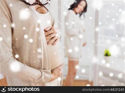 pregnancy, motherhood, winter, people and expectation concept - close up of happy pregnant woman looking to mirror at home over snow