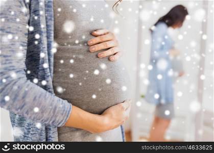 pregnancy, motherhood, winter, people and expectation concept - close up of happy pregnant woman with big belly looking to mirror at home over snow