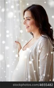 pregnancy, motherhood, winter, people and expectation concept - close up of happy pregnant woman with big belly at window over snow