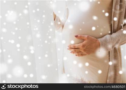 pregnancy, motherhood, winter, people and expectation concept - close up of pregnant woman belly and hands over snow