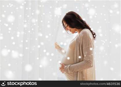 pregnancy, motherhood, winter, people and expectation concept - happy pregnant woman with big belly at window over snow