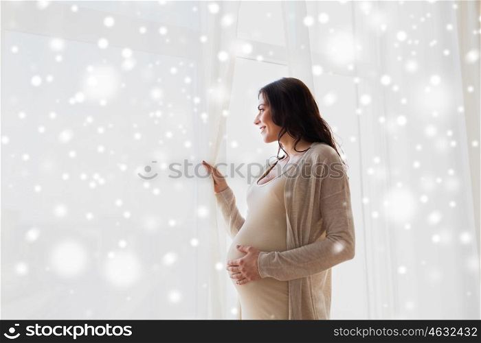pregnancy, motherhood, winter, people and expectation concept -happy pregnant woman with big belly looking trough window over snow