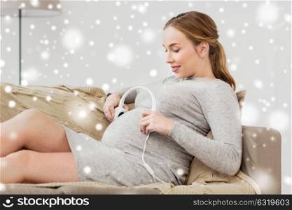 pregnancy, music and people concept - happy pregnant woman holding headphones at her belly at home over snow. pregnant woman holding headphones at her belly