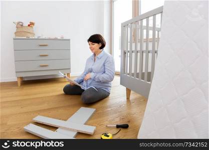 pregnancy, nursery and people concept - single middle-aged pregnant woman with user manual assembling baby bed at home. pregnant woman with manual assembling baby bed