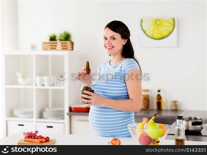 pregnancy, nutrition and people concept - happy pregnant woman eating pickles at home kitchen. pregnant woman eating pickles at home kitchen