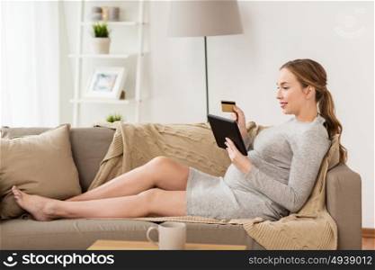 pregnancy, online shopping, technology and people concept - happy pregnant woman with tablet pc computer and credit card at home. pregnant woman with tablet pc and credit card