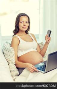 pregnancy, online shopping, technology and people concept - happy pregnant woman with laptop computer and credit card at home