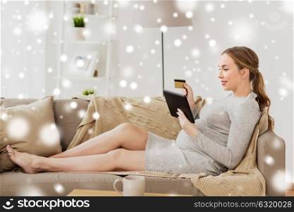 pregnancy, online shopping, technology and people concept - happy pregnant woman with tablet pc computer and credit card at home over snow. pregnant woman with tablet pc and credit card