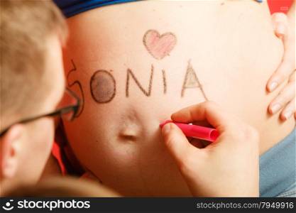 Pregnancy, parenthood and happiness concept. Family expecting new baby, having fun, man painting name of unborn baby girl writing on belly of pregnant woman