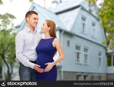 pregnancy, parenthood, housing, real estate and people concept - happy young family expecting child looking at each other over living house background outdoors