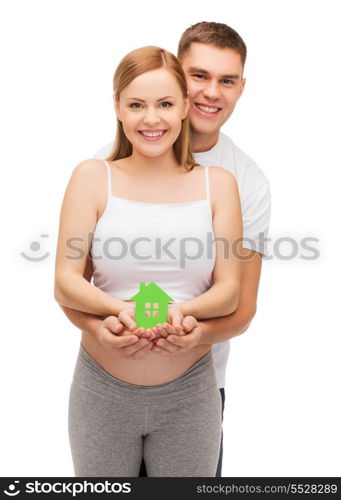 pregnancy, parenthood, real estate and happiness concept - happy young family expecting child showing green paper house