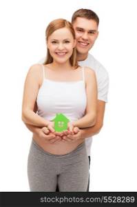 pregnancy, parenthood, real estate and happiness concept - happy young family expecting child showing green paper house
