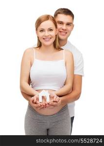 pregnancy, parenthood, real estate and happiness concept - happy young family expecting child showing white paper house