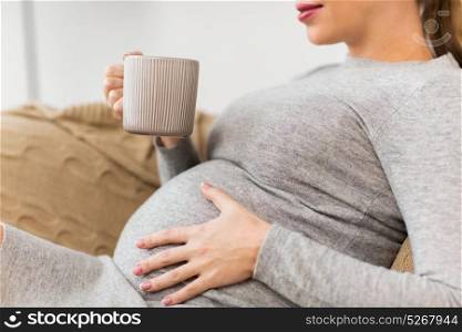 pregnancy, people and expectation concept - close up of happy pregnant woman with cup drinking tea at home. happy pregnant woman with cup drinking tea at home
